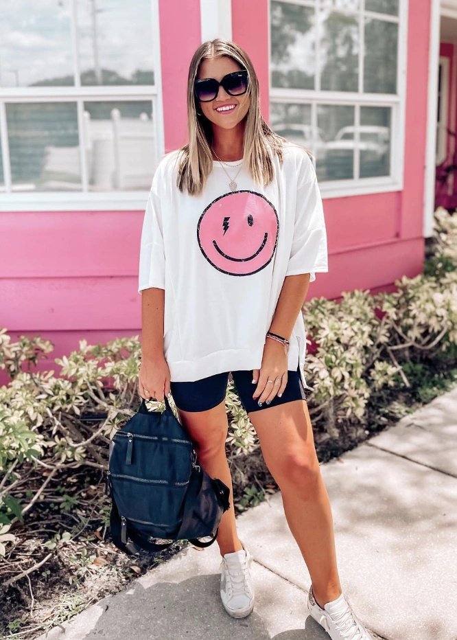Oversized white graphic tee with smiley face, paired with black biker shorts. Casual style, perfect for summer outings or relaxed events.