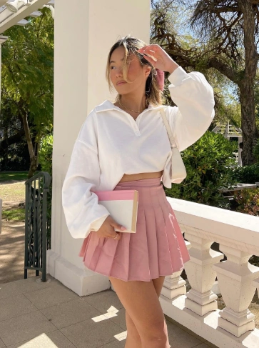 Casual outfit featuring a white cropped pullover and a pink pleated tennis skirt, ideal for warm weather outings.