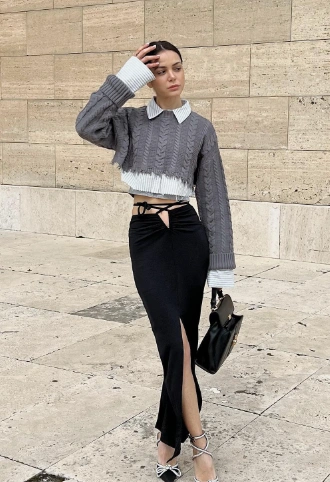 Black maxi skirt featuring a high slit, paired with a gray cropped cable-knit sweater. Suitable for casual outings or stylish events.
