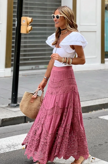 A casual crochet maxi skirt in pink with intricate patterns, paired with a white off-the-shoulder top, ideal for summer outings.