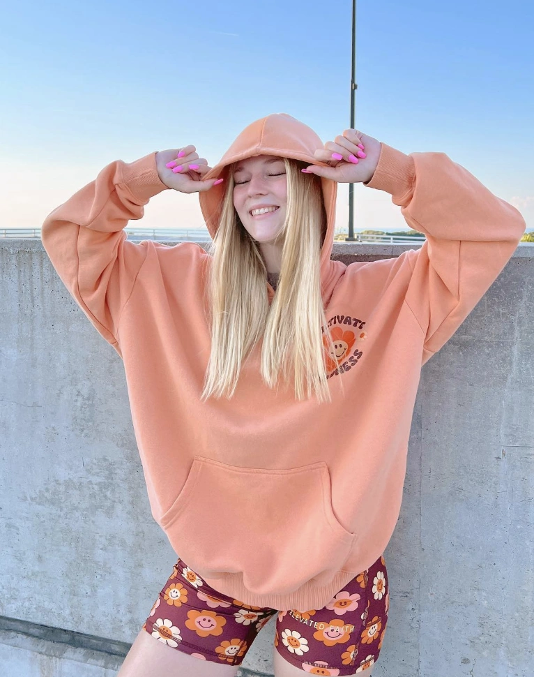Oversized peach hoodie with a front pocket and graphic, paired with maroon shorts featuring cheerful floral patterns; ideal for casual outings.