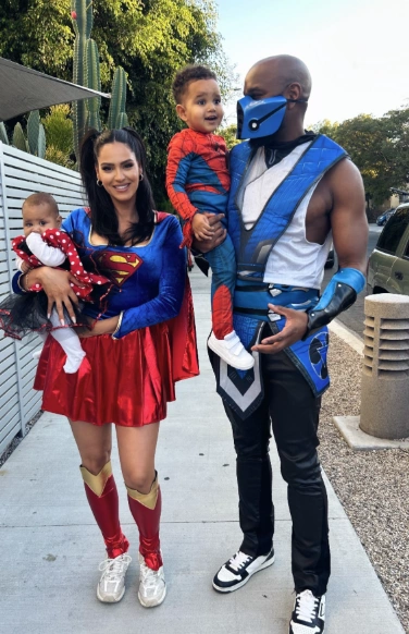 Family in superhero costumes: woman in a blue and red dress with cape, man in blue armor, kids in matching outfits. Ideal for Halloween festivities.