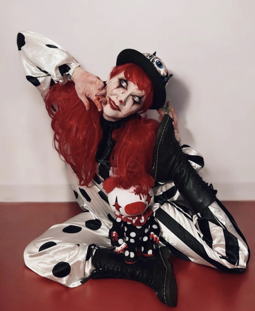A playful clown costume featuring shiny black and white stripes, oversized sleeves, and polka dots, perfect for Halloween or themed parties.