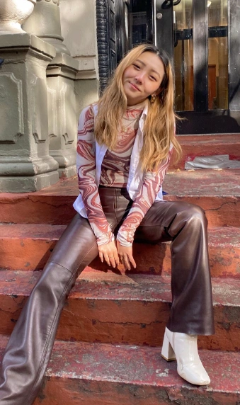 Brown leather pants paired with a marbled long-sleeve top and white heeled booties, perfect for casual outings.