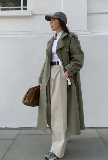 Olive green trench coat layered over a white shirt, paired with beige wide-leg trousers and stylish sneakers, perfect for casual outings.