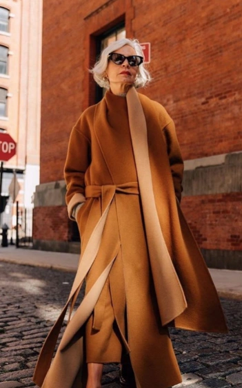 A long camel wrap coat featuring an asymmetrical design, wide sleeves, and a belted waist, perfect for formal occasions.