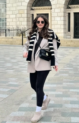 Relaxed maternity outfit featuring a light beige oversized blazer, black leggings, and a striped sweater draped over shoulders, ideal for casual outings.