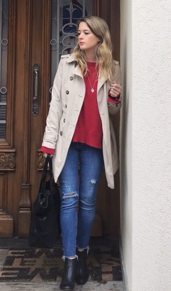 A casual winter outfit featuring a red sweater, beige trench coat, distressed blue jeans, and ankle boots, perfect for everyday wear.