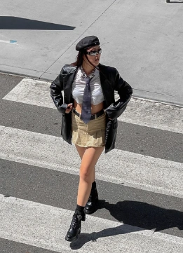 A stylish outfit featuring a cropped white shirt, beige mini skirt, and black leather blazer, ideal for casual outings.