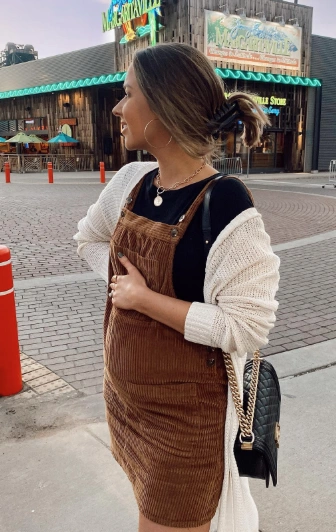 Casual brown corduroy dress layered over a black top, paired with a white cardigan; perfect for autumn outings.