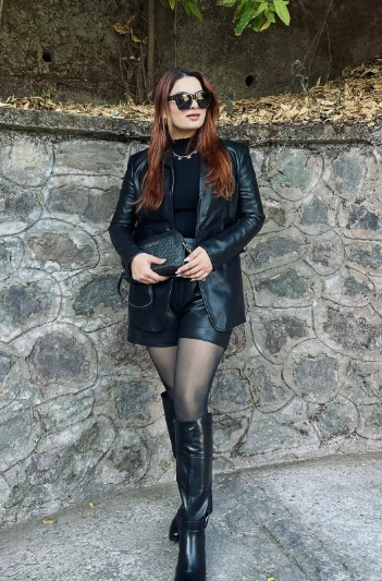 A chic black outfit featuring a fitted blazer, high-waisted shorts, and knee-high boots, perfect for a night out.
