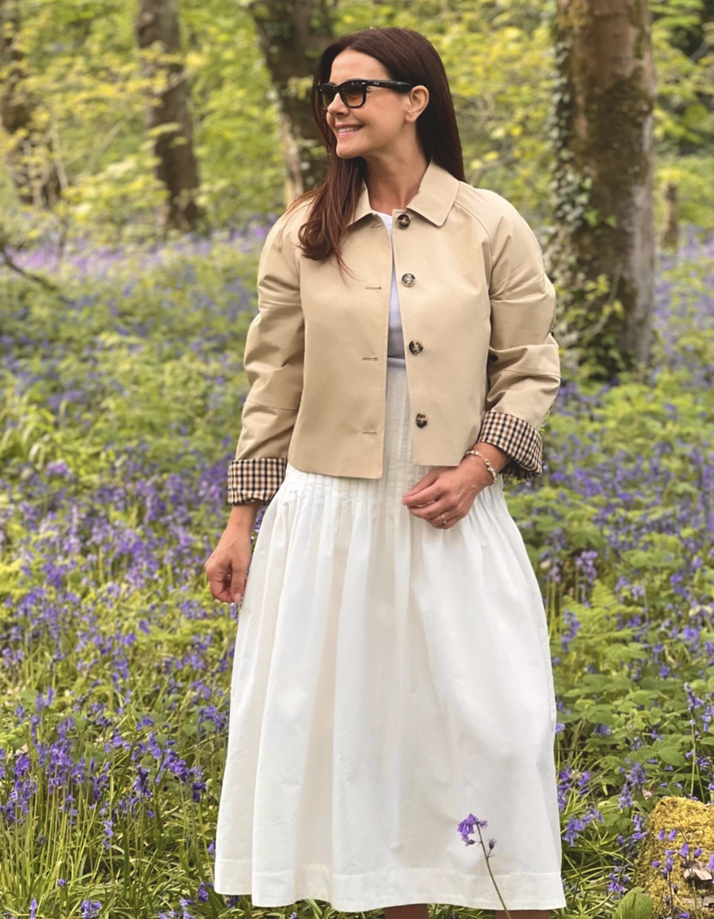 Beige cropped jacket with checked cuffs worn over a white midi dress, set against a purple wildflower garden backdrop.