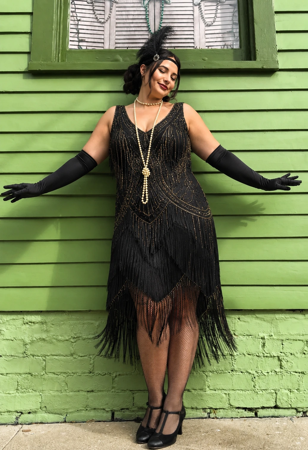 Black beaded flapper dress with fringe, long gloves, pearl necklace, and T-strap heels against green siding.