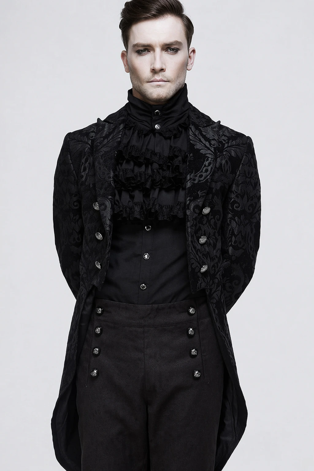 Black brocade jacket, high-neck ruffled shirt, and buttoned trousers create a dark, aristocratic menswear look.