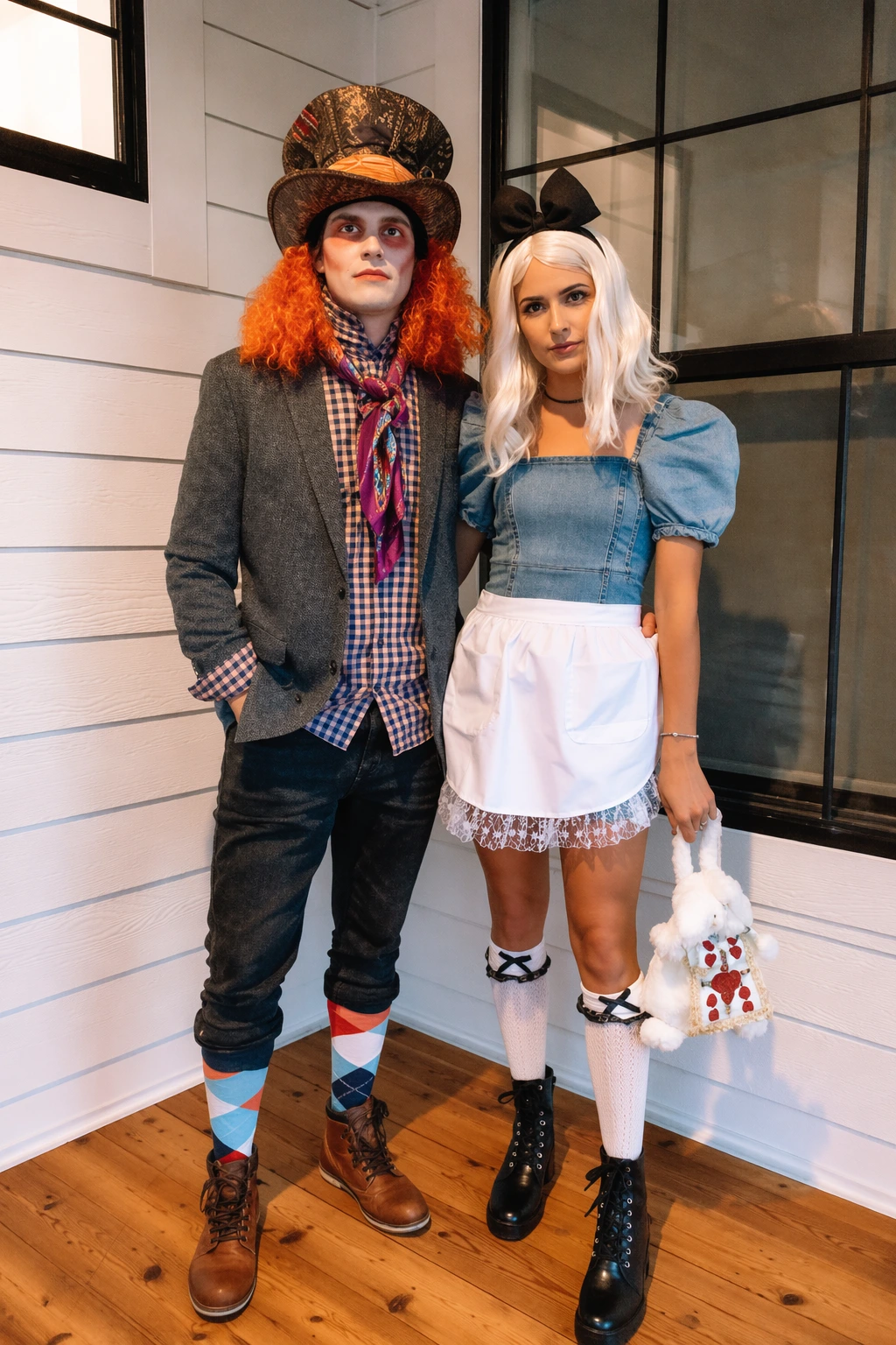 Two people in whimsical Halloween costumes, one as a Mad Hatter with orange curls, tall hat, and mismatched socks.