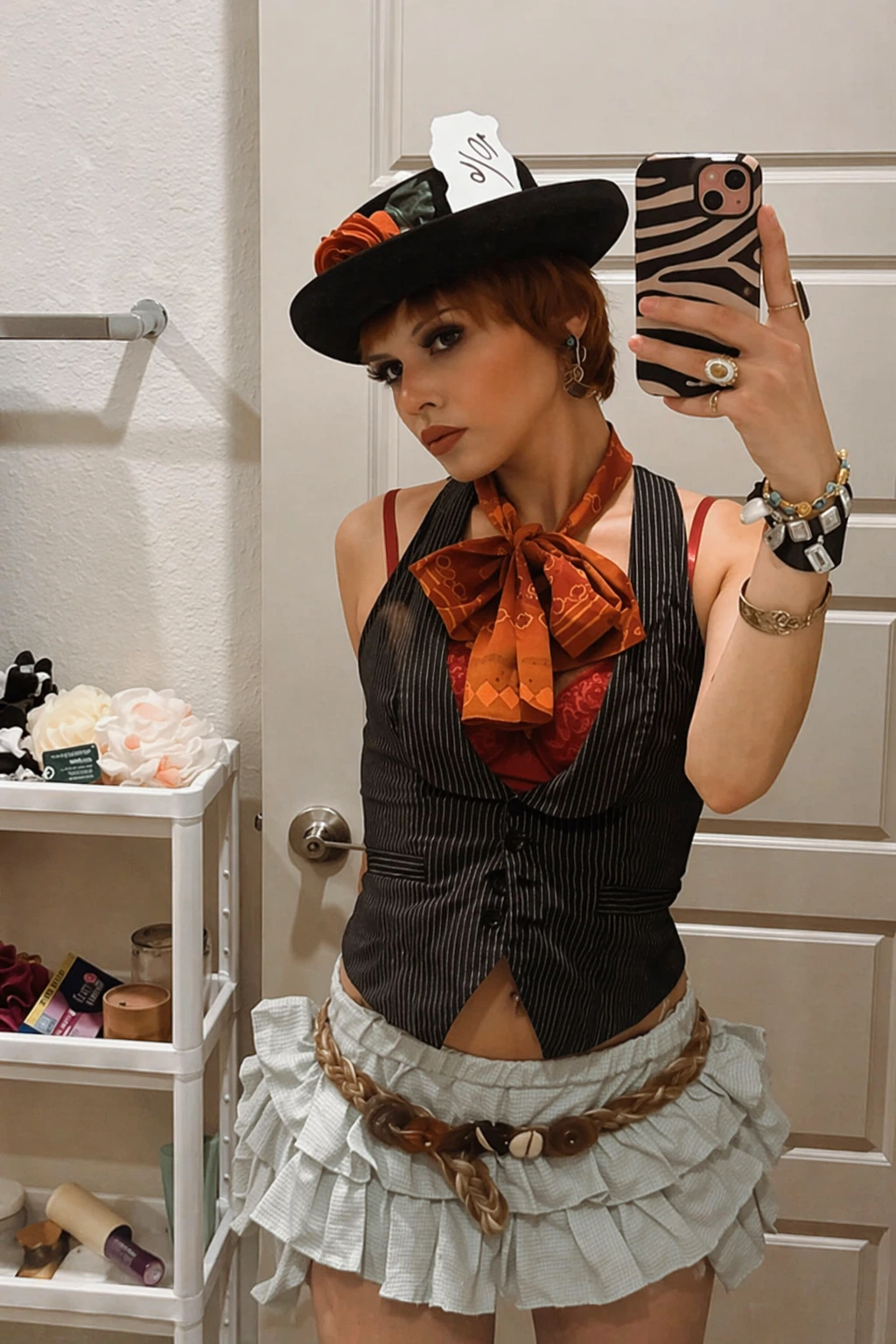 Short auburn hair, zebra phone case selfie, black pinstripe vest, orange neck bow, and pale ruffled mini skirt.