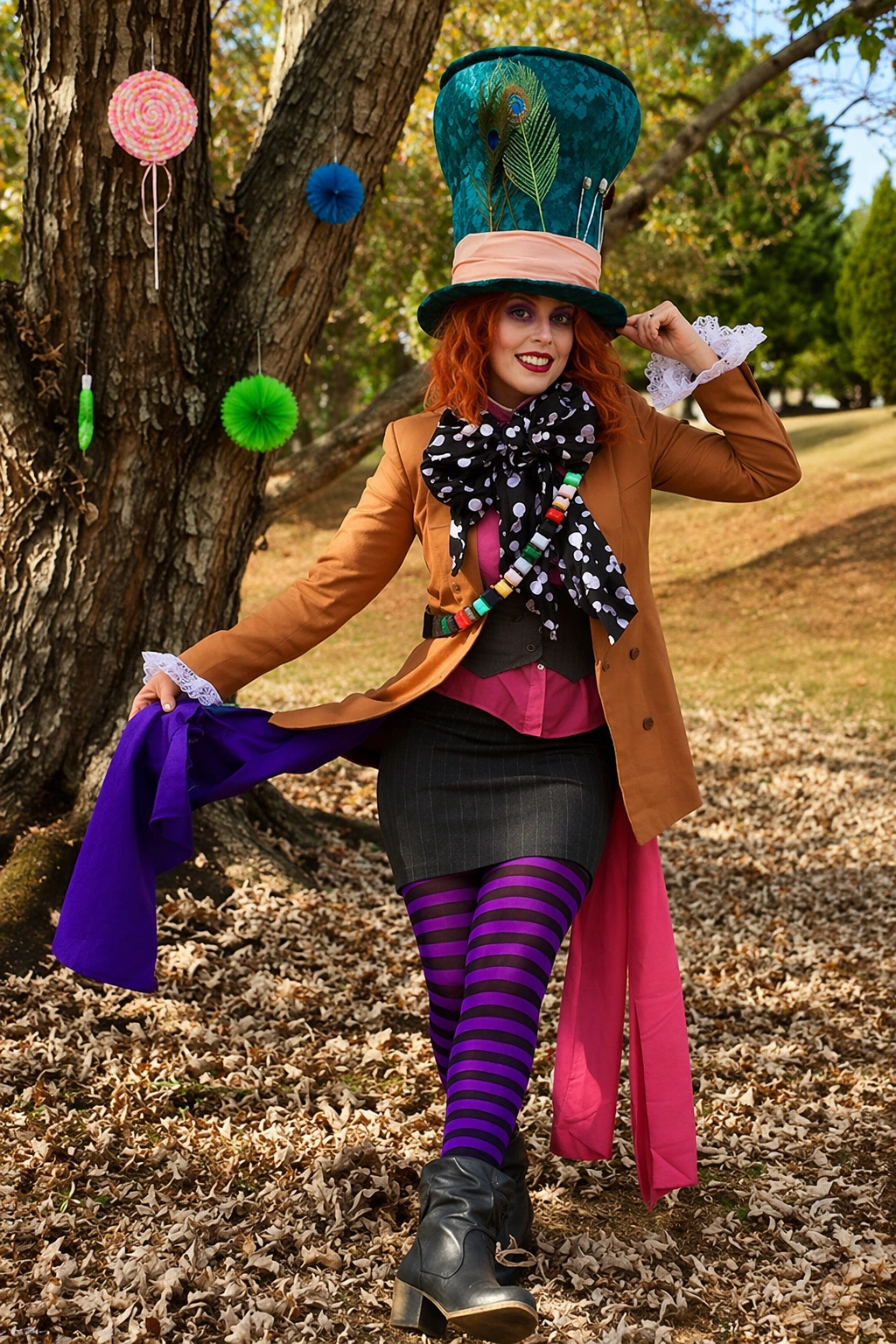 Woman standing by a tree in a teal top hat, striped tights, tan jacket, and bold scarf.