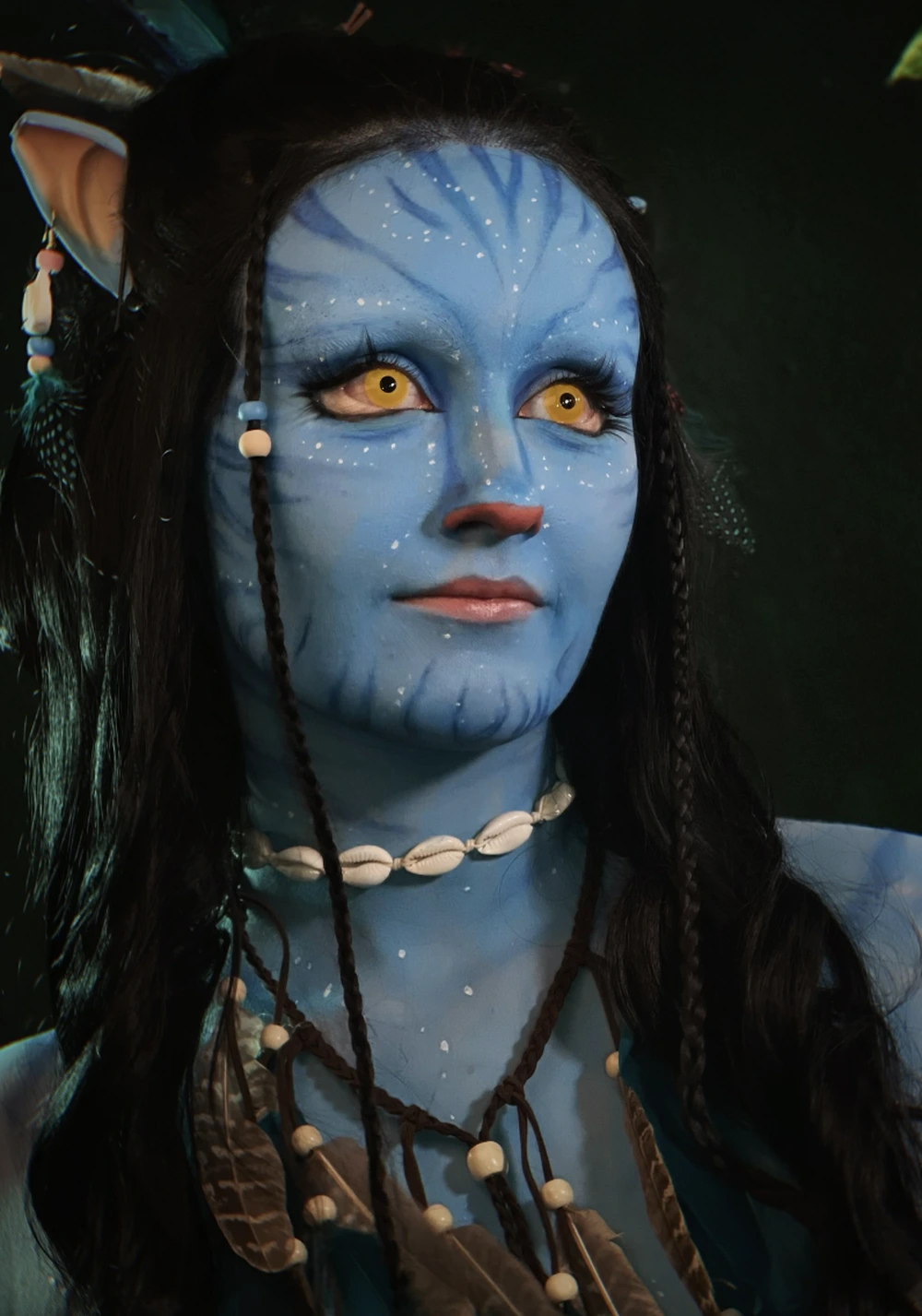 Blue-skinned avatar with yellow eyes, braided hair, shell necklace, and white speckled facial markings in dark lighting.