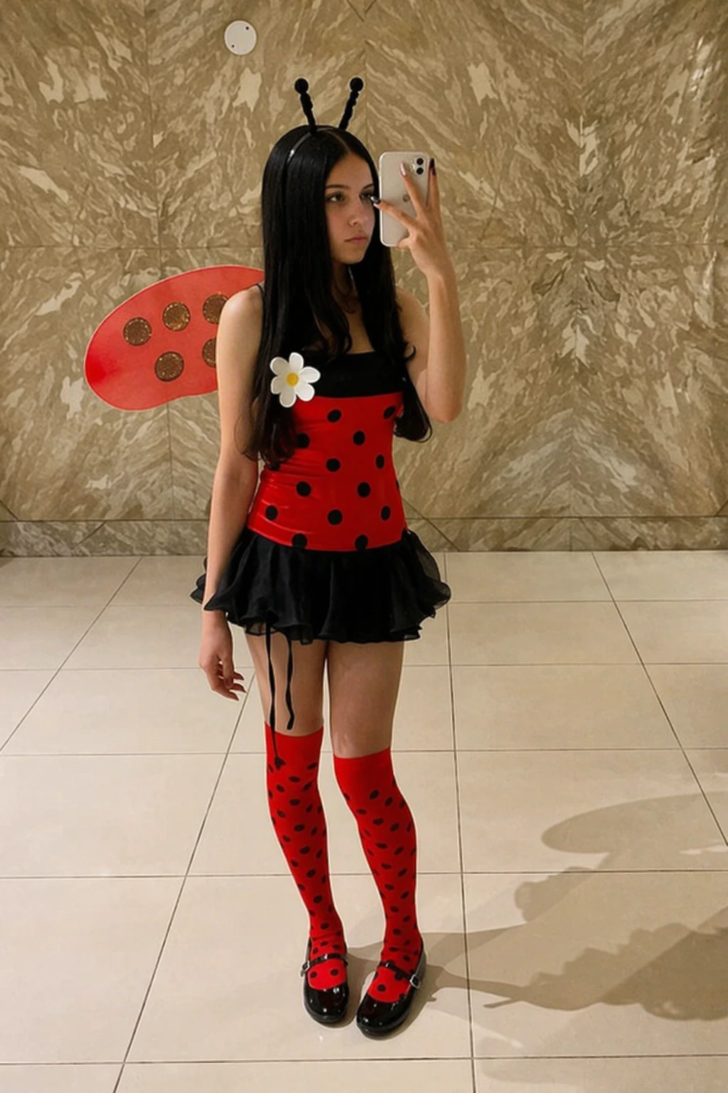 Teen girl takes a mirror selfie wearing a red polka-dot ladybug costume with black skirt and antenna headband.
