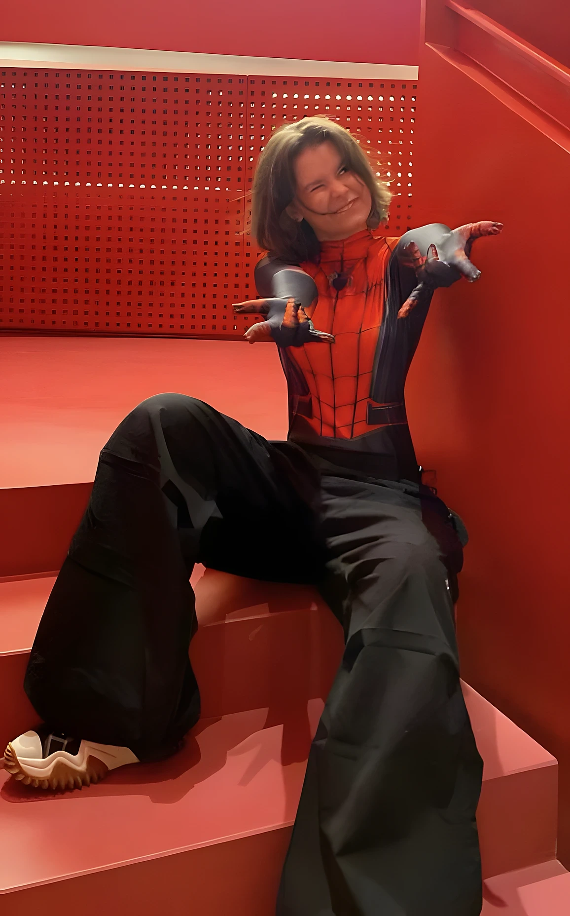 Child seated on red steps in Spider-Man costume, black pants, smiling pose, and dramatic lighting.