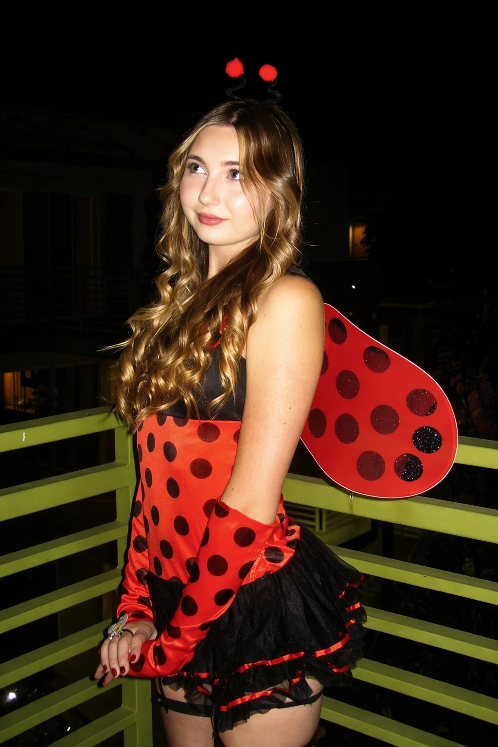 Woman in a red polka-dot ladybug costume poses on a balcony, wearing wings, gloves, and antenna headband.