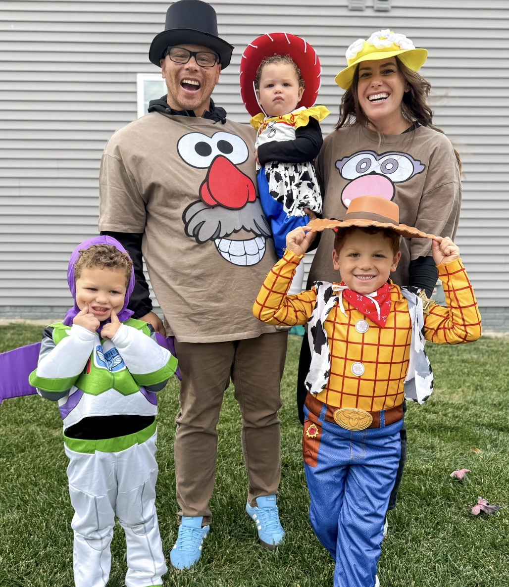 Adults and children wear Mr. Potato Head shirts, Woody costume, and Buzz Lightyear outfit on a lawn.