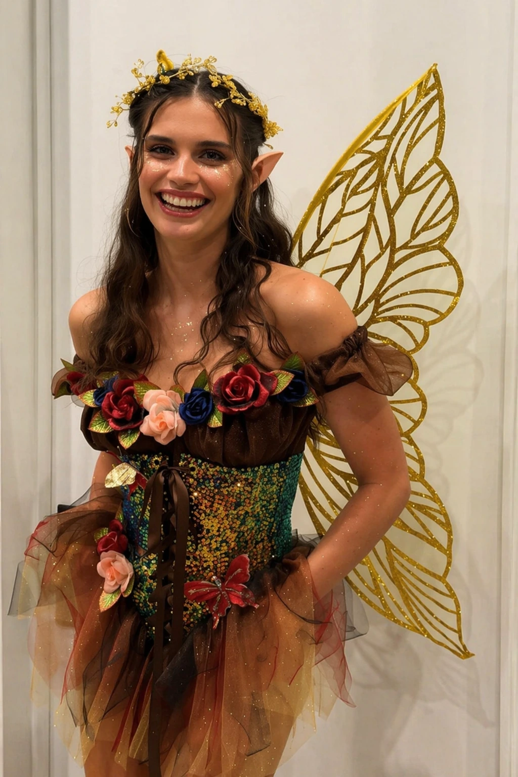 Smiling woman in brown floral fairy costume, glittery bodice, pointed ears, gold leaf-pattern wings.