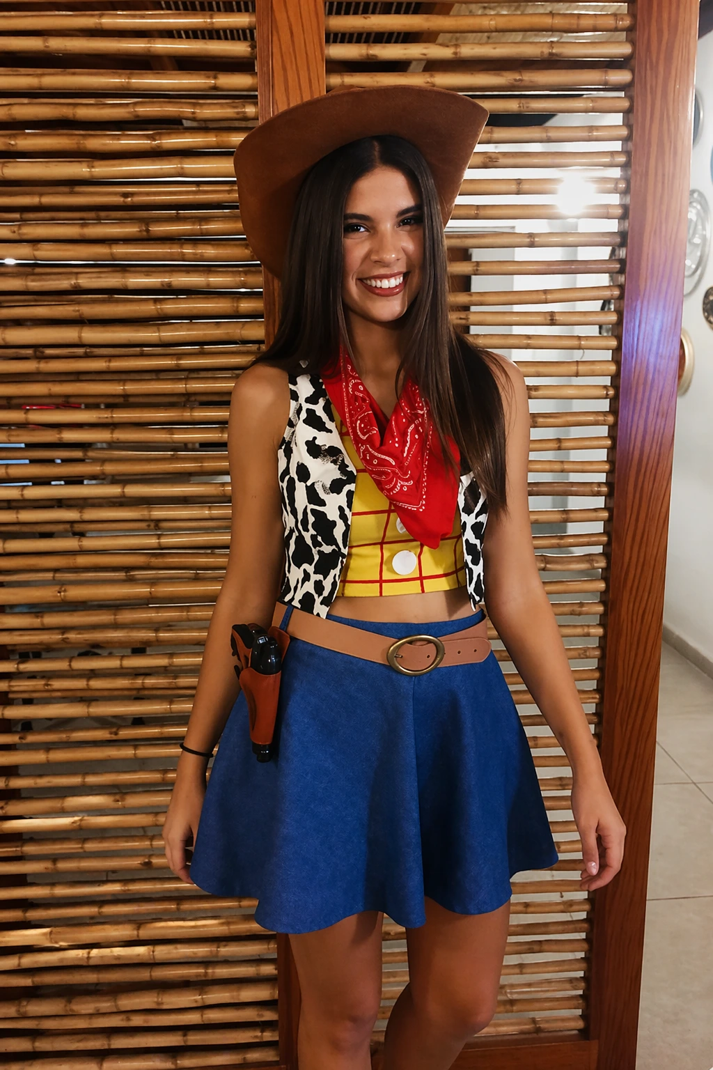 Woman in Woody-inspired costume with brown hat, cow-print vest, red bandana, blue skirt, and toy holster.