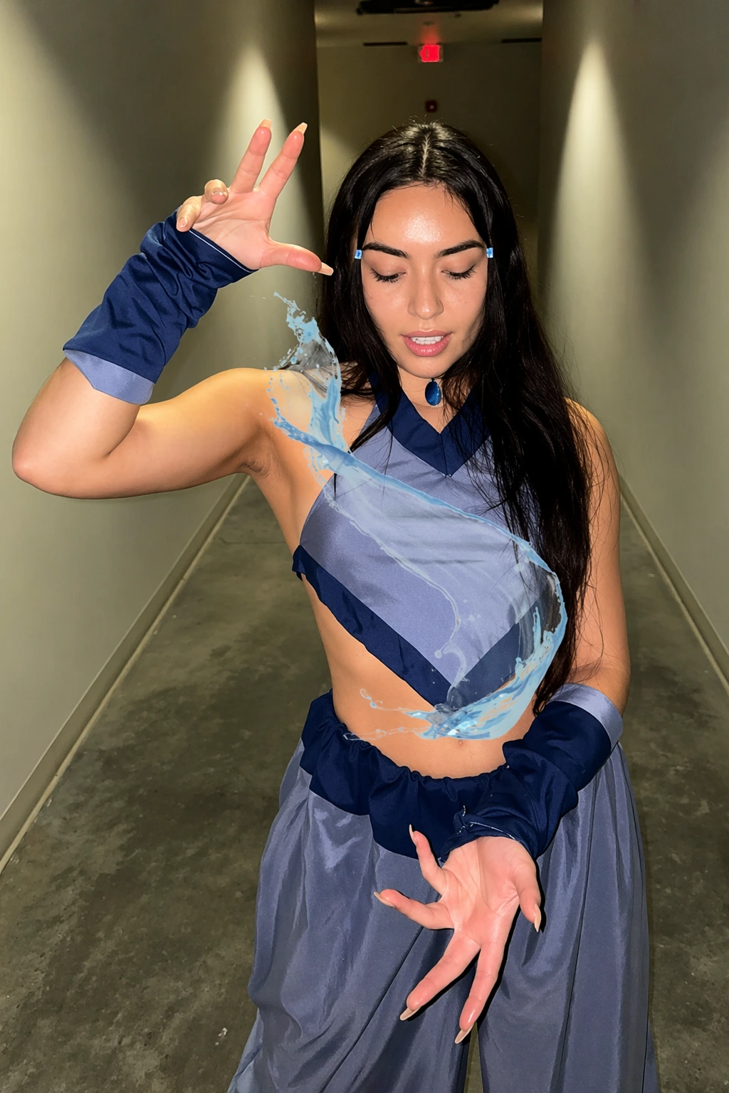 Young woman in blue and gray Katara-style outfit, long black hair, wrist guards, and water effect overlay indoors.