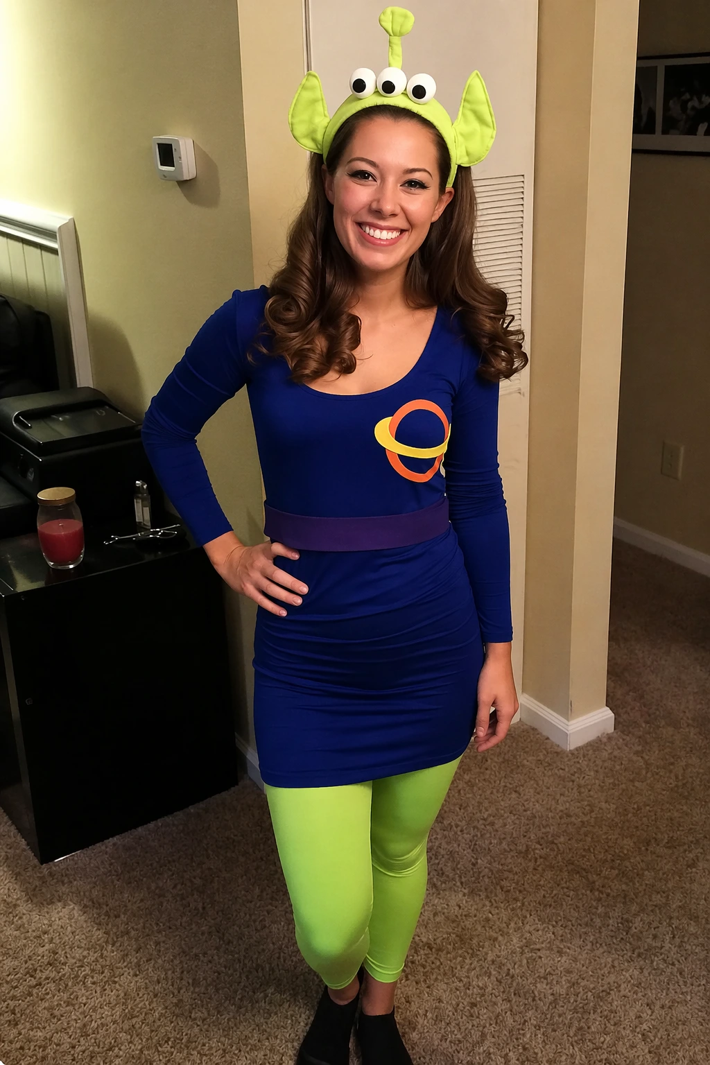Smiling woman indoors wearing a lime green alien headband, blue dress, neon leggings, and black socks.