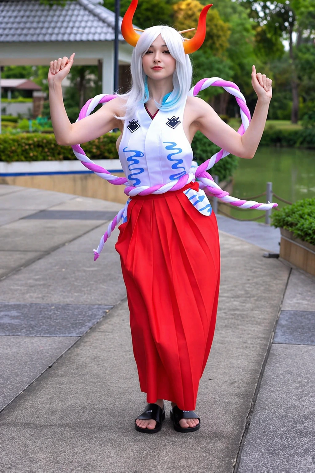 White-haired cosplayer with orange horns, twisted rope accessories, red skirt, and sleeveless top outdoors.