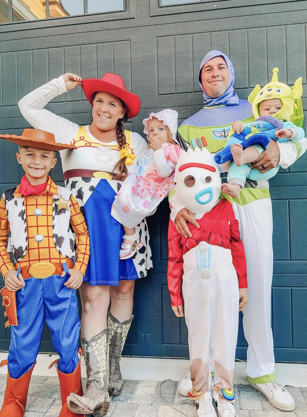 Family group poses in Toy Story costumes with Woody, Jessie, Buzz, Bo Peep, and alien-themed baby outfits.