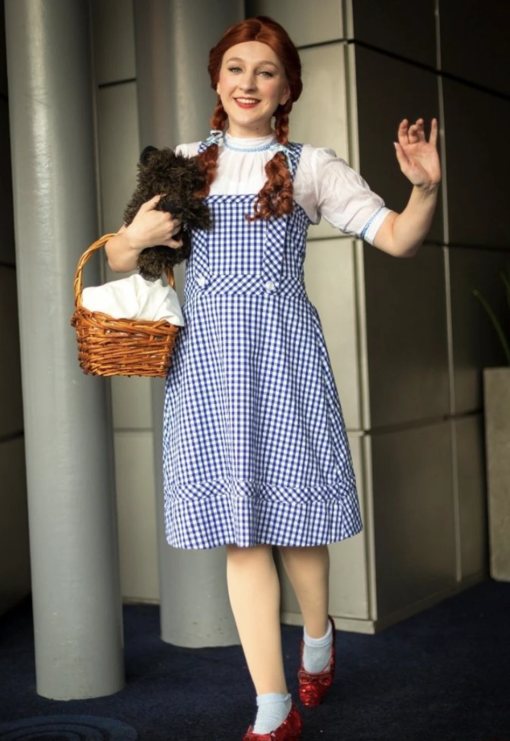 Woman dressed as Dorothy in a blue gingham dress, braided red hair, basket, and glittery red shoes.