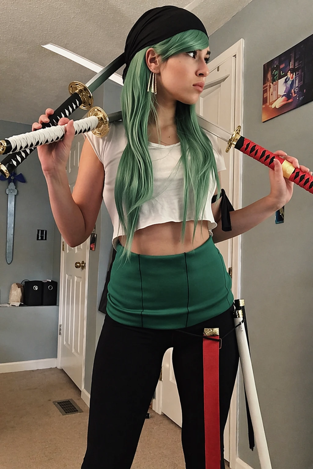 Cosplayer with mint green hair, cropped white top, black leggings, and three katana props in a bedroom setting.