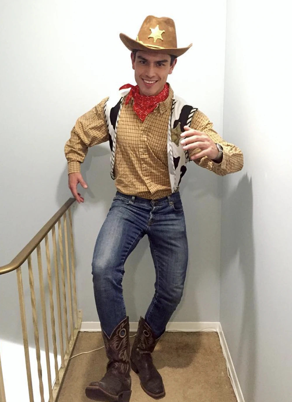 Smiling man in Woody outfit, cowboy hat, red bandana, plaid shirt, jeans, and boots.