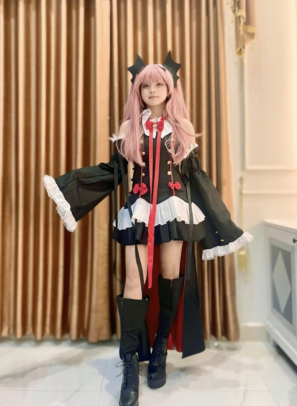 Pink wig, black-and-red fantasy outfit, bat wing headpiece, long sleeves, thigh boots, and indoor curtain backdrop.