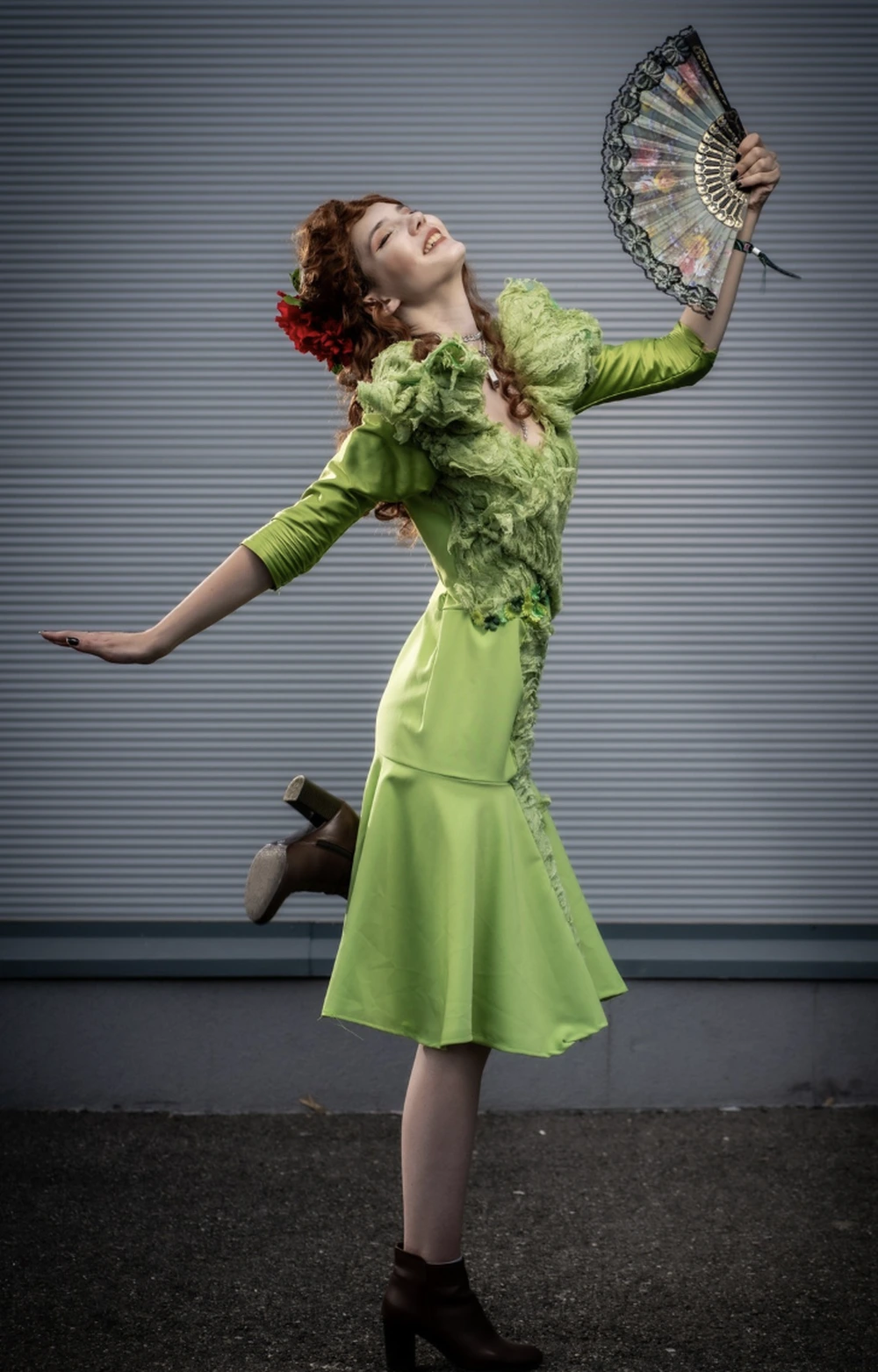 Red-haired woman in vivid green dress with ruffled trim, holding fan, posed in theatrical stance.